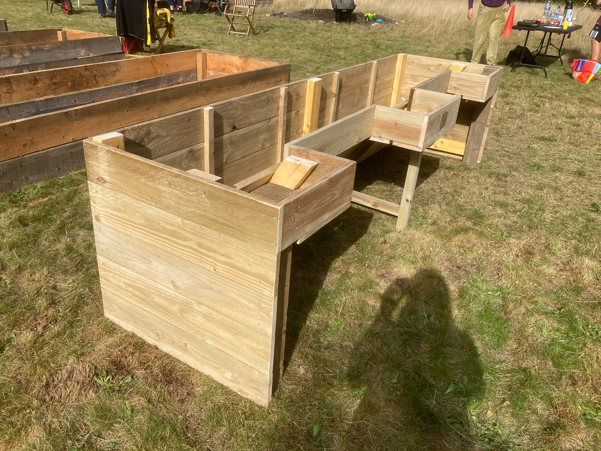 An accessible raised bed made from light wood, not containing soil. The bed is rectangular with two openings for chairs or wheelchairs.