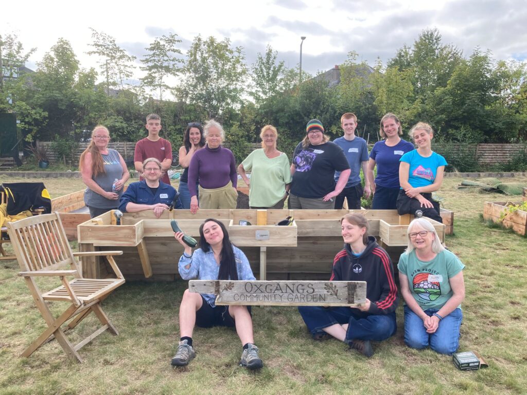 Volunteers standing behind and sitting in front of an accessible raised bed they built. Two people are holding a sign for the community garden